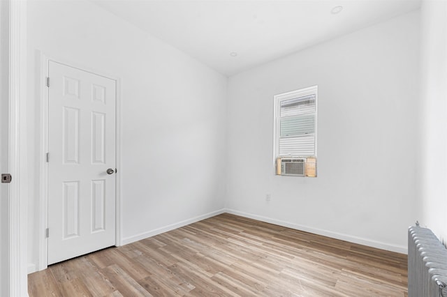 unfurnished room with cooling unit, baseboards, radiator, and light wood-style flooring