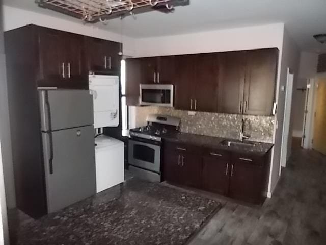 kitchen featuring dark brown cabinetry, sink, stainless steel appliances, stacked washing maching and dryer, and backsplash