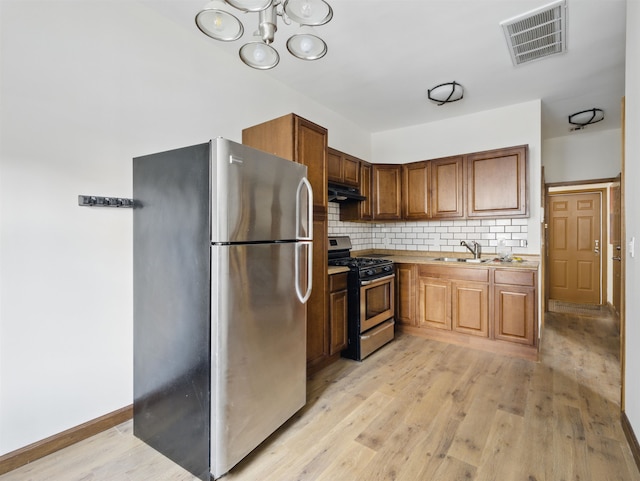kitchen with under cabinet range hood, light wood-style floors, visible vents, appliances with stainless steel finishes, and a sink