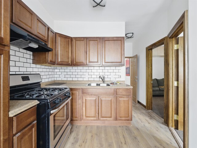kitchen with light wood-type flooring, light countertops, stainless steel range with gas cooktop, under cabinet range hood, and a sink