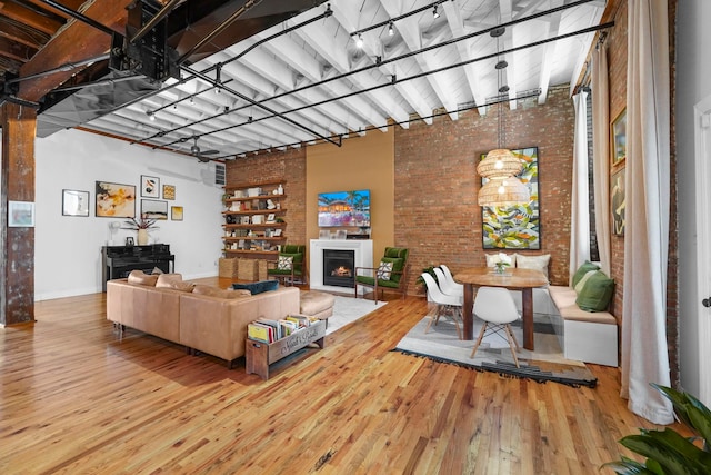 living area featuring track lighting, a warm lit fireplace, brick wall, and hardwood / wood-style flooring