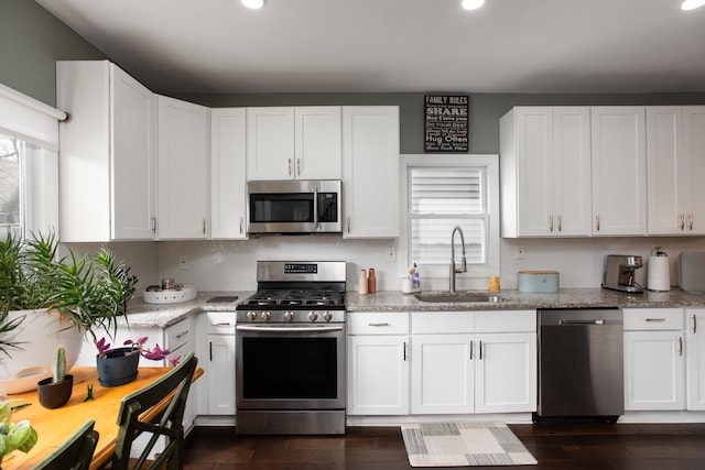 kitchen with light stone counters, appliances with stainless steel finishes, white cabinets, and a sink