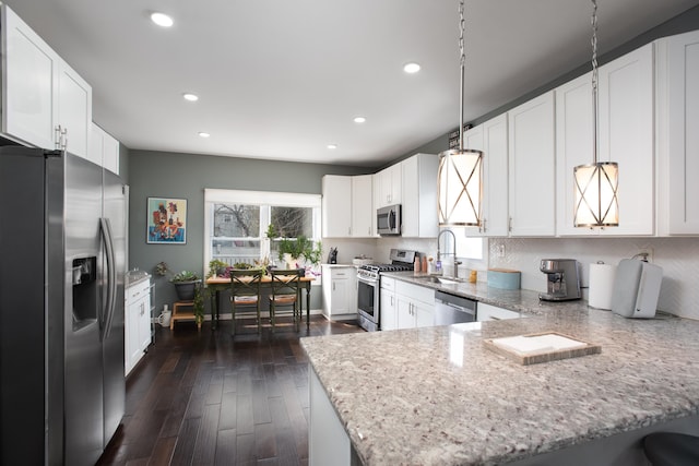 kitchen featuring light stone counters, appliances with stainless steel finishes, white cabinetry, a sink, and a peninsula