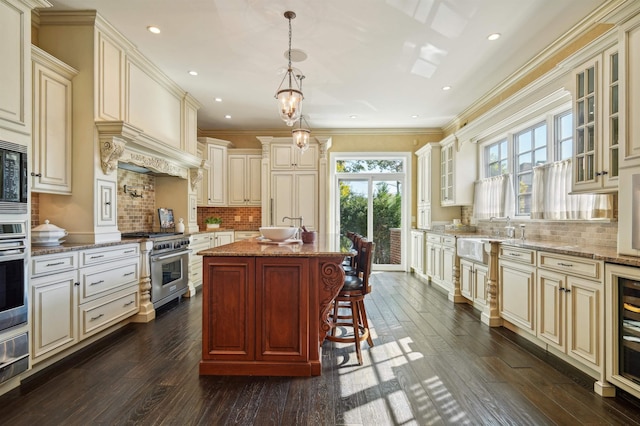 kitchen with a kitchen breakfast bar, hanging light fixtures, appliances with stainless steel finishes, cream cabinetry, and glass insert cabinets