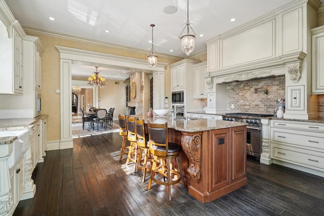 kitchen with stainless steel stove, a kitchen breakfast bar, hanging light fixtures, light stone countertops, and a center island with sink