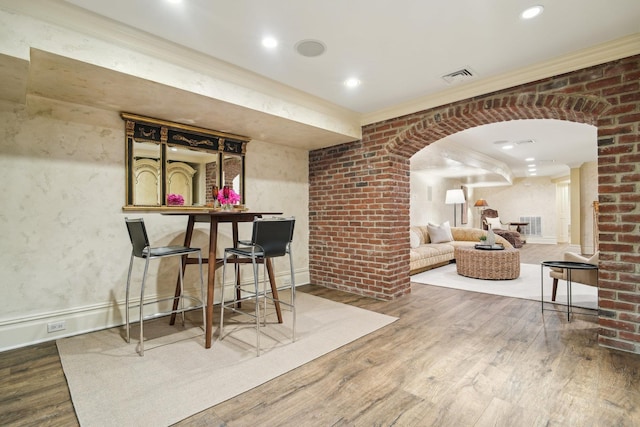 bar featuring arched walkways, crown molding, visible vents, brick wall, and wood finished floors