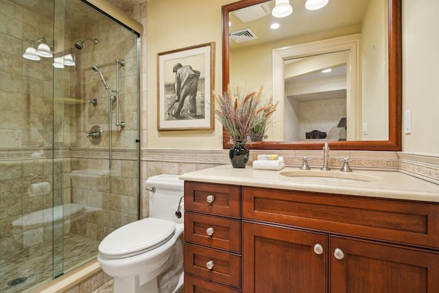 bathroom featuring toilet, a wainscoted wall, vanity, visible vents, and a stall shower