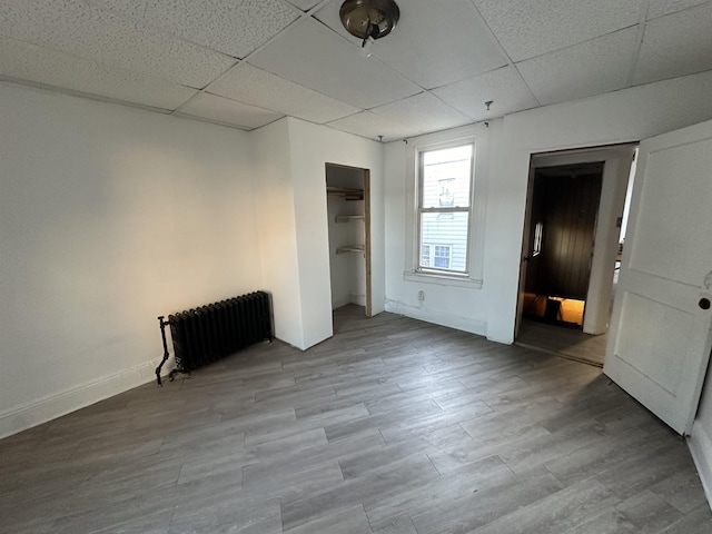 spare room with a paneled ceiling, light wood finished floors, and radiator heating unit