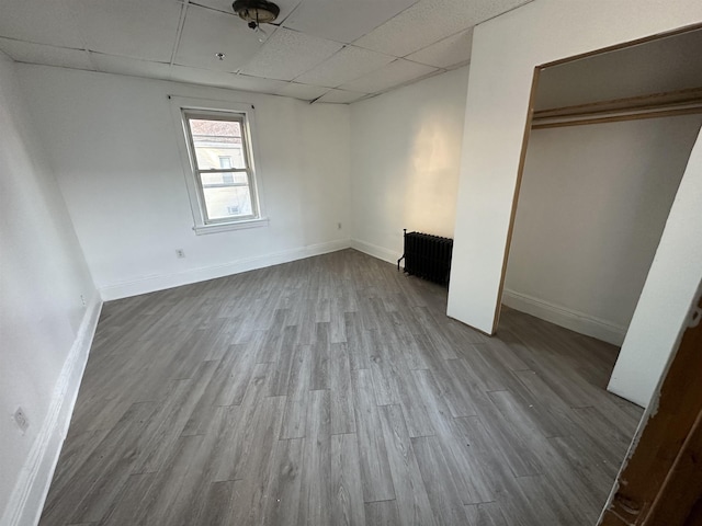 unfurnished bedroom featuring light wood-type flooring, a paneled ceiling, radiator, and baseboards