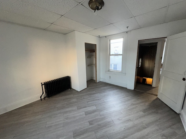 spare room featuring a paneled ceiling, radiator heating unit, baseboards, and light wood-style flooring