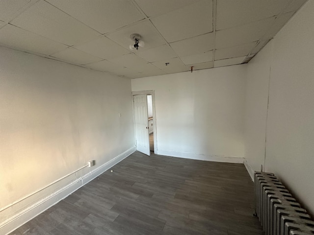 spare room with dark wood-style flooring, radiator heating unit, a paneled ceiling, and baseboards