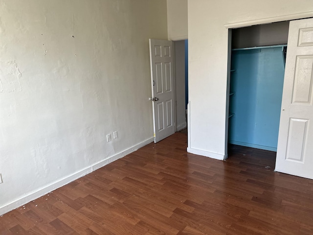 unfurnished bedroom featuring dark wood-style flooring, a closet, and baseboards