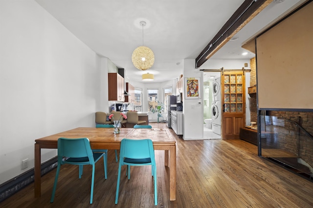 dining area with a barn door, baseboards, wood finished floors, and stacked washer / drying machine