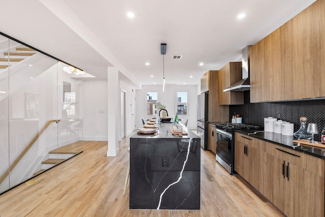 kitchen featuring dark countertops, appliances with stainless steel finishes, a kitchen island with sink, modern cabinets, and wall chimney exhaust hood