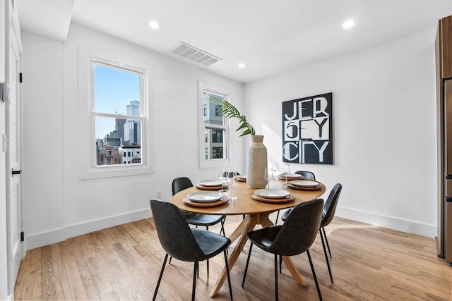 dining room with light wood-style floors, baseboards, a view of city, and visible vents