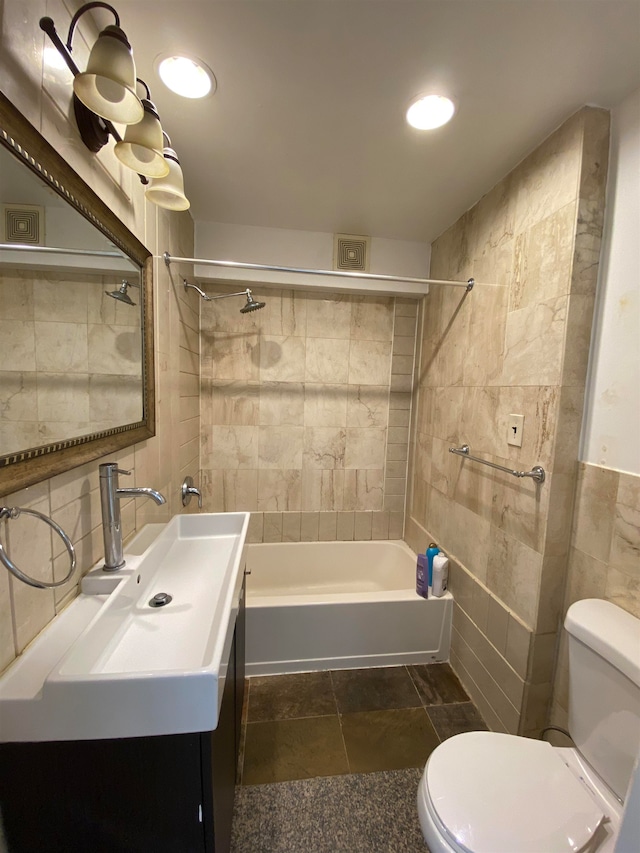 full bathroom with tile walls, tile patterned floors, vanity, tiled shower / bath combo, and toilet