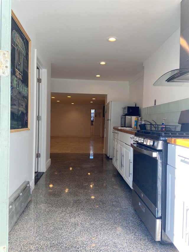 kitchen with white cabinets, stainless steel range with gas stovetop, wall chimney range hood, and white refrigerator