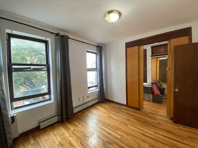 unfurnished bedroom with light wood-type flooring, multiple windows, and a baseboard radiator