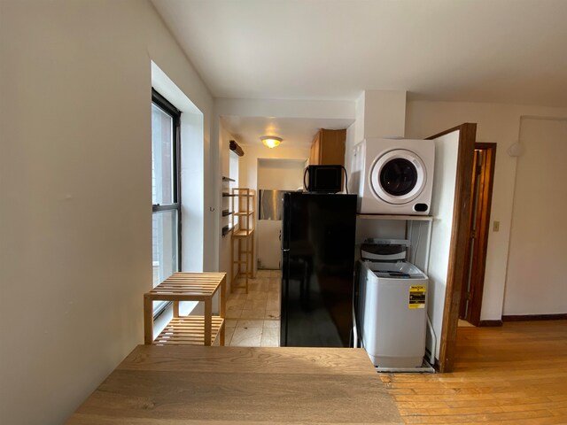 kitchen with black appliances, stacked washer and clothes dryer, and light wood-type flooring