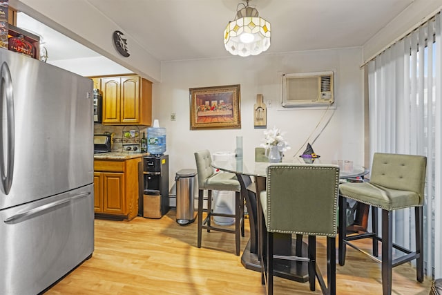 kitchen with light wood finished floors, backsplash, a wall mounted AC, brown cabinetry, and freestanding refrigerator