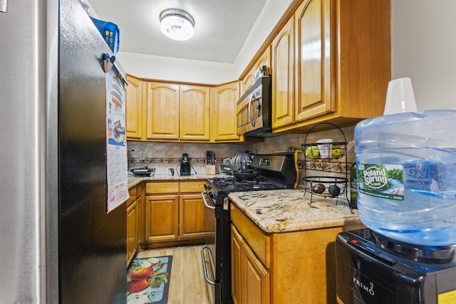 kitchen with decorative backsplash, appliances with stainless steel finishes, brown cabinets, light stone counters, and light wood-style floors