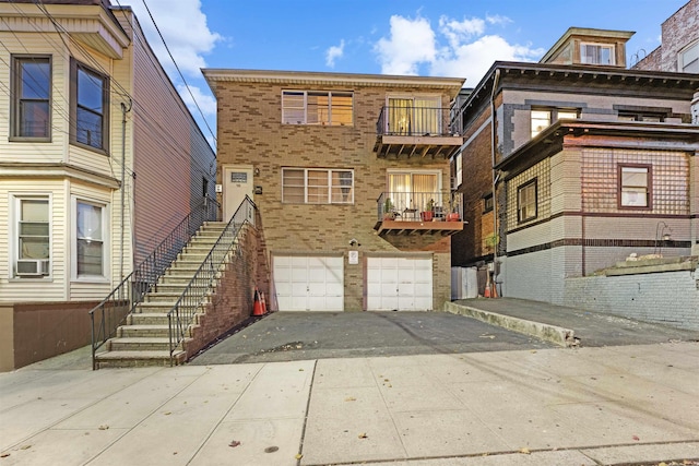 back of property with aphalt driveway, brick siding, an attached garage, cooling unit, and stairs