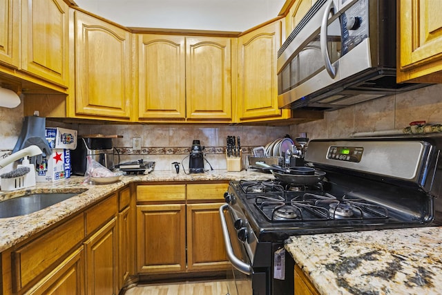 kitchen with light stone counters, brown cabinets, backsplash, appliances with stainless steel finishes, and a sink