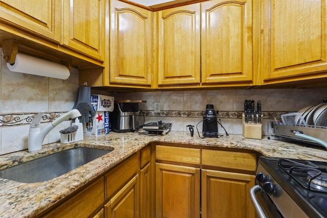 kitchen featuring light stone counters, stainless steel range with gas cooktop, a sink, and backsplash