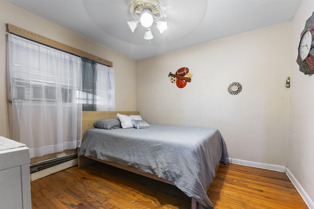 bedroom with a ceiling fan, baseboards, baseboard heating, and wood finished floors