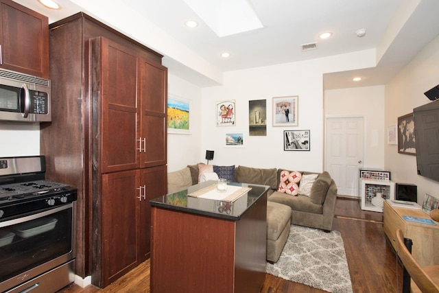 kitchen with stainless steel appliances, a kitchen island, a skylight, and dark wood-type flooring