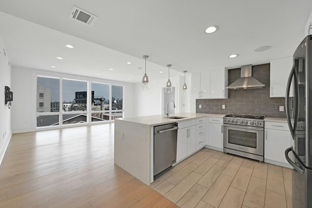 kitchen with stainless steel appliances, a sink, visible vents, wall chimney range hood, and backsplash