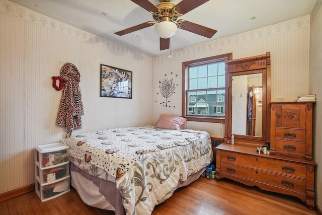 bedroom featuring wood-type flooring, baseboards, a ceiling fan, and wallpapered walls