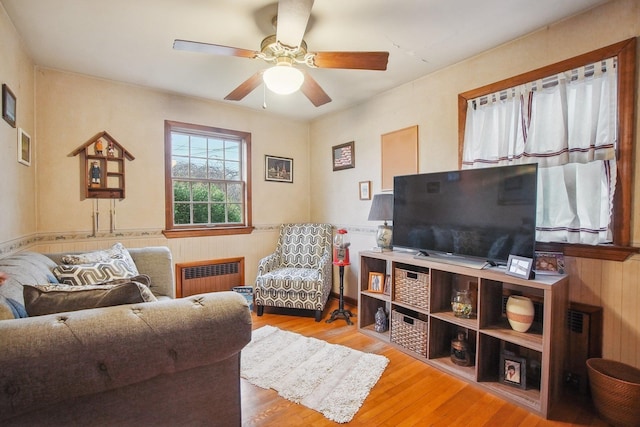 living room with a ceiling fan, radiator, wood walls, and wood finished floors