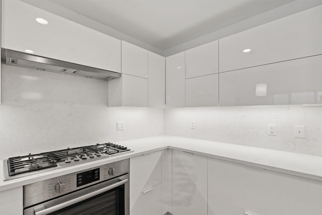 kitchen featuring wall chimney range hood, backsplash, white cabinets, and appliances with stainless steel finishes