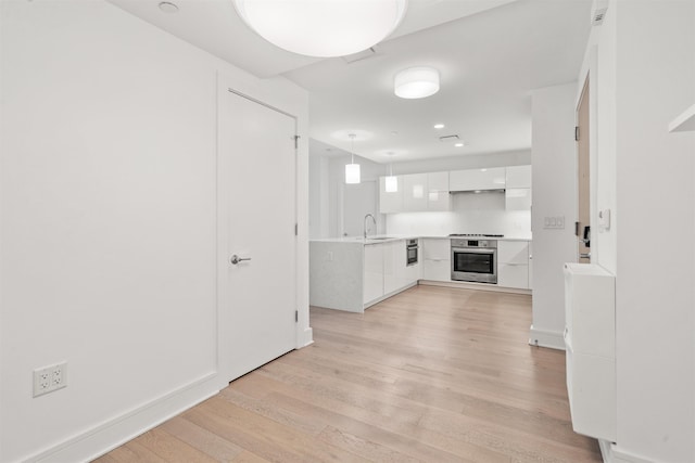 kitchen with sink, hanging light fixtures, light hardwood / wood-style floors, white cabinets, and oven