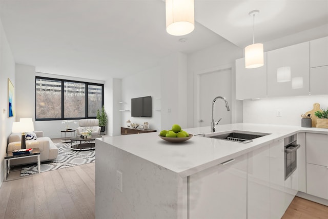 kitchen with white cabinetry, sink, decorative light fixtures, and light hardwood / wood-style floors