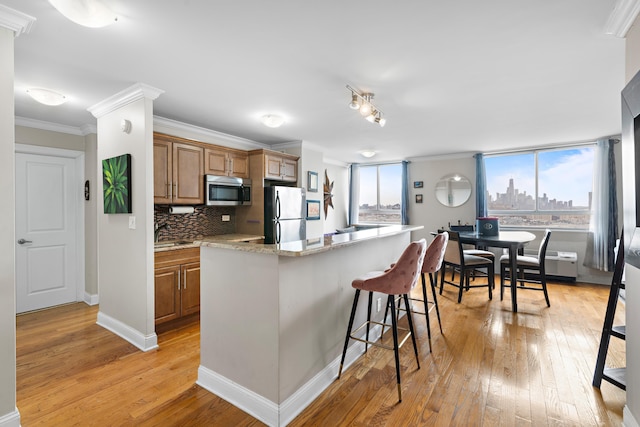 100 Manhattan Ave Unit 407, Union City, NJ 07087 - kitchen with stainless steel appliances, light wood finished floors, a kitchen breakfast bar, crown molding, and brown cabinets