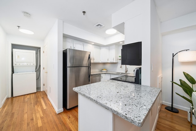kitchen with appliances with stainless steel finishes, stacked washer / drying machine, light stone counters, and white cabinets