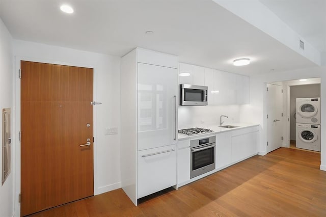 99 Hudson St Unit 401, Jersey City, NJ 07302 - kitchen with stainless steel appliances, stacked washer / dryer, a sink, white cabinets, and light wood-style flooring