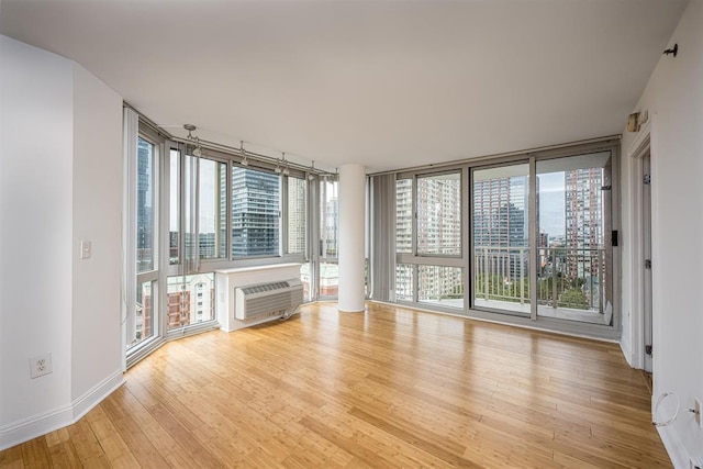 unfurnished living room featuring light hardwood / wood-style flooring, an AC wall unit, and a wall of windows