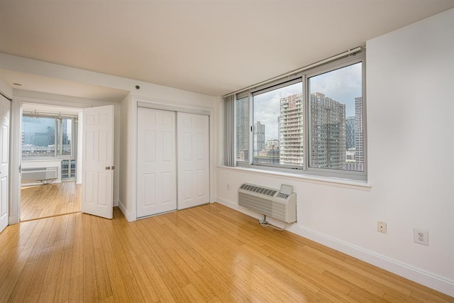 unfurnished bedroom featuring a wall mounted air conditioner, multiple windows, light hardwood / wood-style floors, and a closet