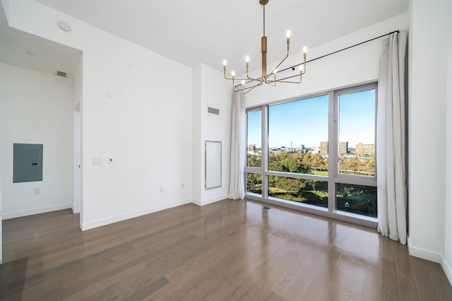 empty room featuring a towering ceiling, electric panel, dark hardwood / wood-style flooring, and a chandelier