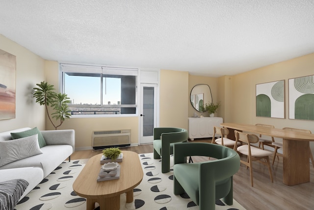 living room with light hardwood / wood-style flooring, a wall mounted air conditioner, and a textured ceiling