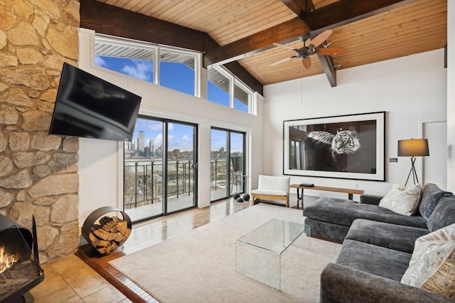 tiled living room featuring vaulted ceiling with beams, ceiling fan, a stone fireplace, and wooden ceiling