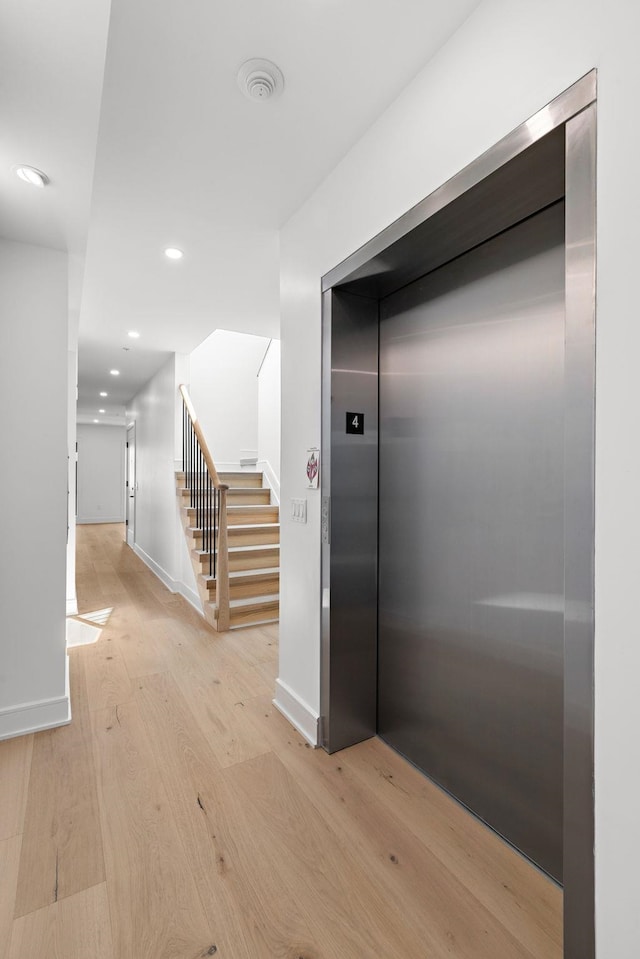 hallway featuring stairs, recessed lighting, light wood-style flooring, baseboards, and elevator