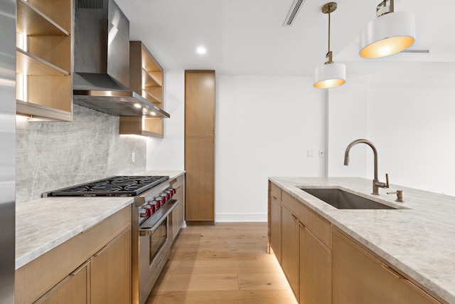 kitchen featuring stainless steel range, a sink, open shelves, wall chimney range hood, and light wood-type flooring