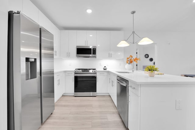 kitchen with appliances with stainless steel finishes, a peninsula, white cabinetry, light countertops, and light wood-style flooring