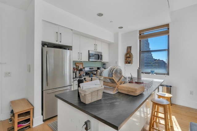 kitchen featuring dark countertops, white cabinets, light wood-style floors, and appliances with stainless steel finishes