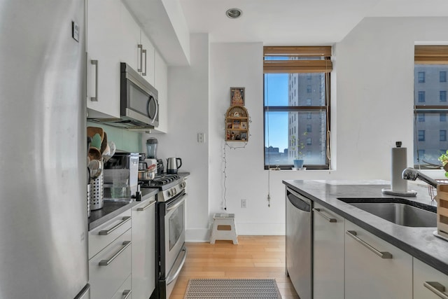 kitchen with light wood-type flooring, a sink, dark countertops, white cabinetry, and appliances with stainless steel finishes