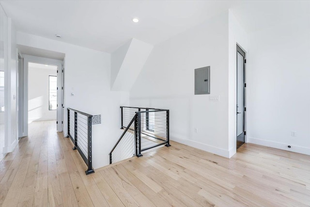 hall featuring light wood-type flooring, electric panel, baseboards, and an upstairs landing